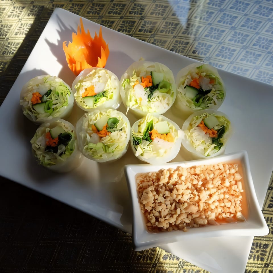 Eight fresh Thai spring rolls with vegetables and a side of peanut sauce on a white plate.