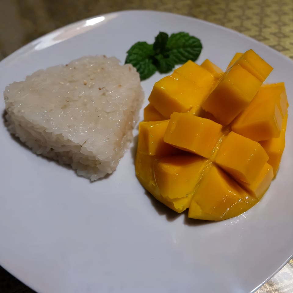Thai mango sticky rice dessert with fresh mint on a white plate.