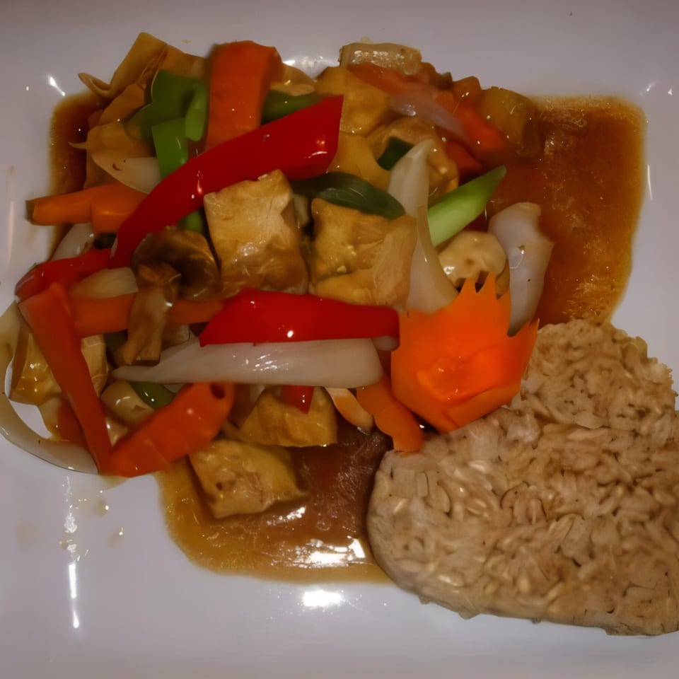Thai stir-fried tofu with colorful vegetables and brown rice on a white plate.