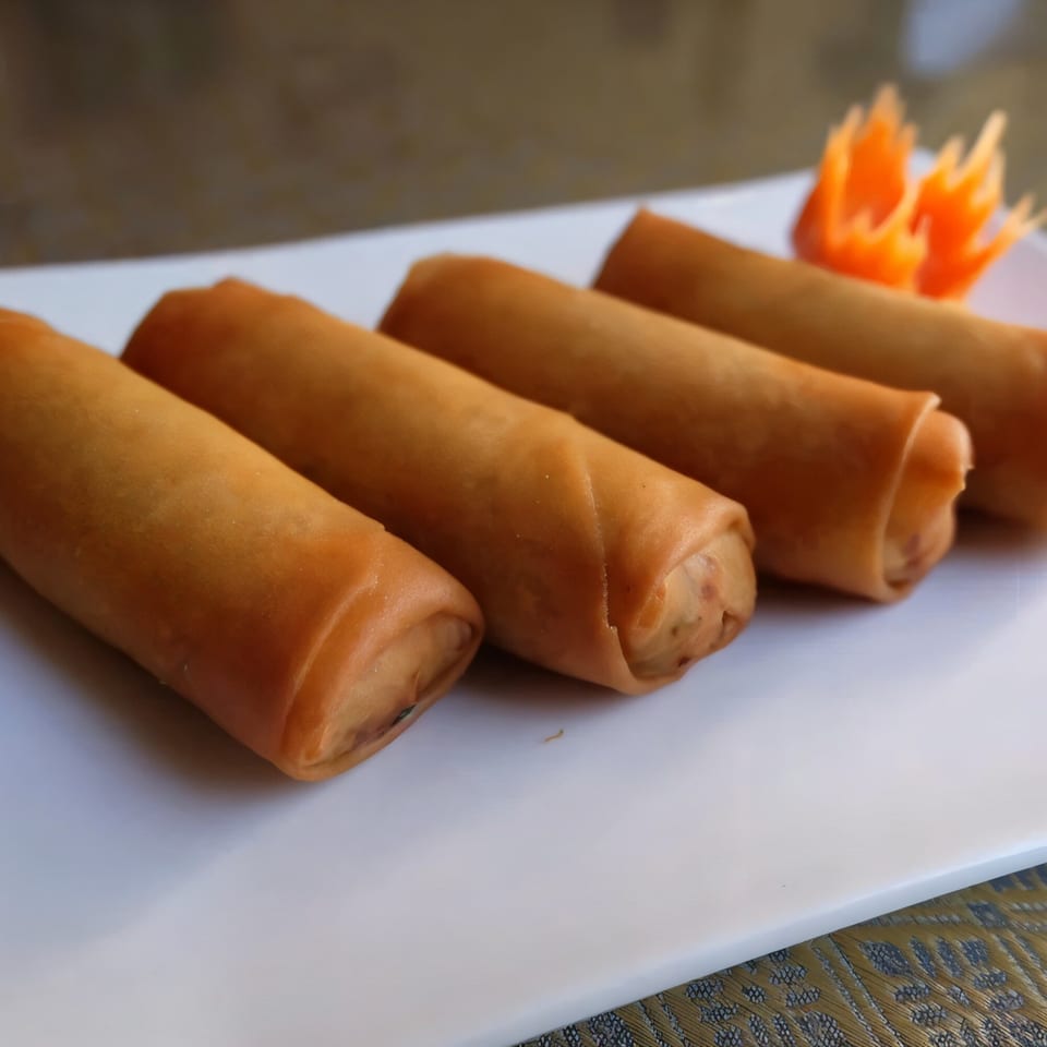 Four crispy Thai spring rolls on a white rectangular plate, garnished with carved carrots.
