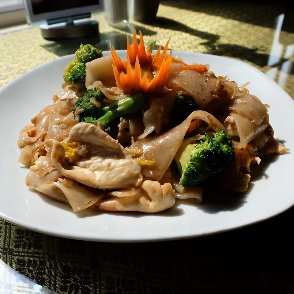 Thai Nakornping's Pad See Ew with wide noodles, broccoli, and a carved carrot garnish.