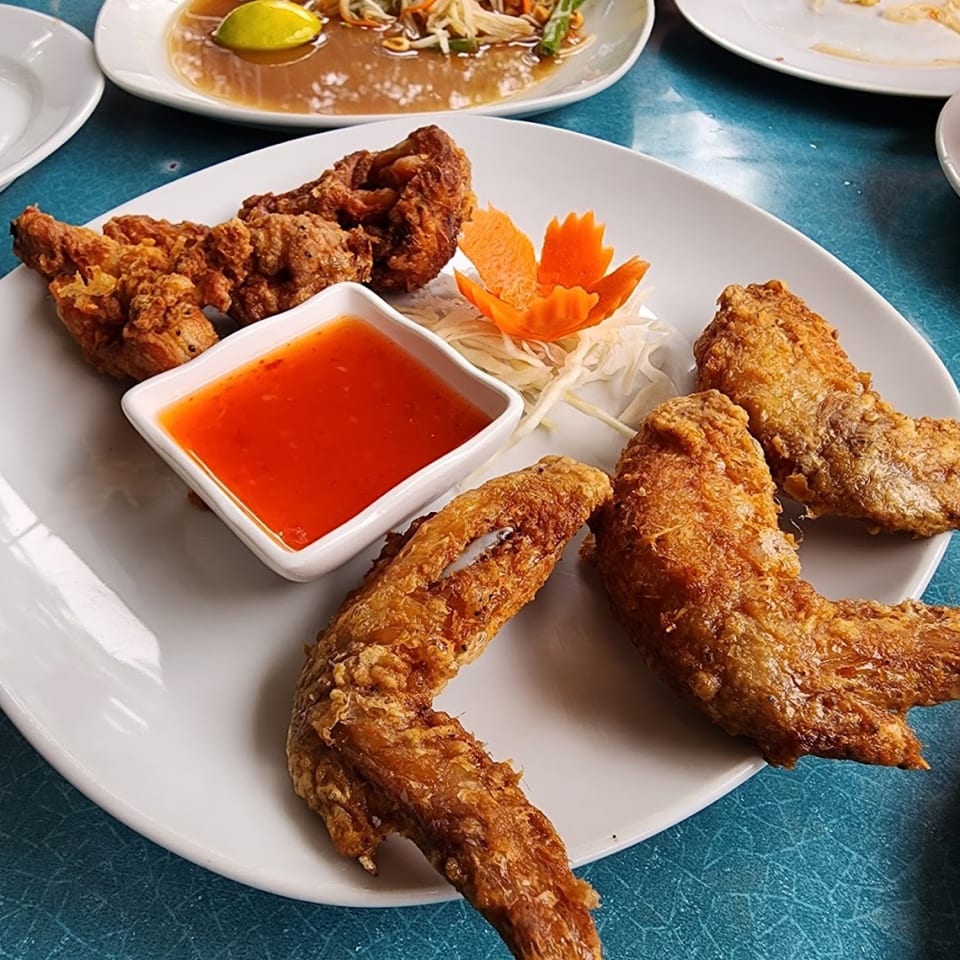 Crispy fried chicken wings with sweet chili dipping sauce and a carrot garnish on a white plate.