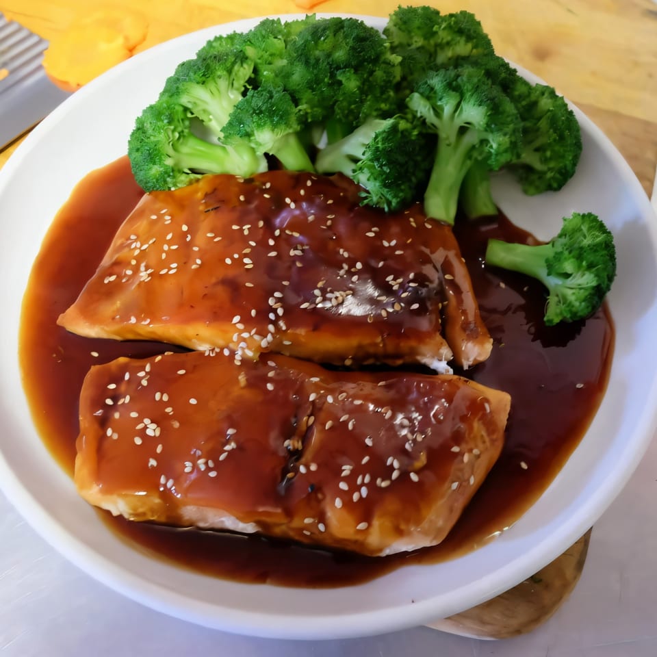 Two salmon fillets with sesame seeds and brown sauce, served with steamed broccoli on a white plate.