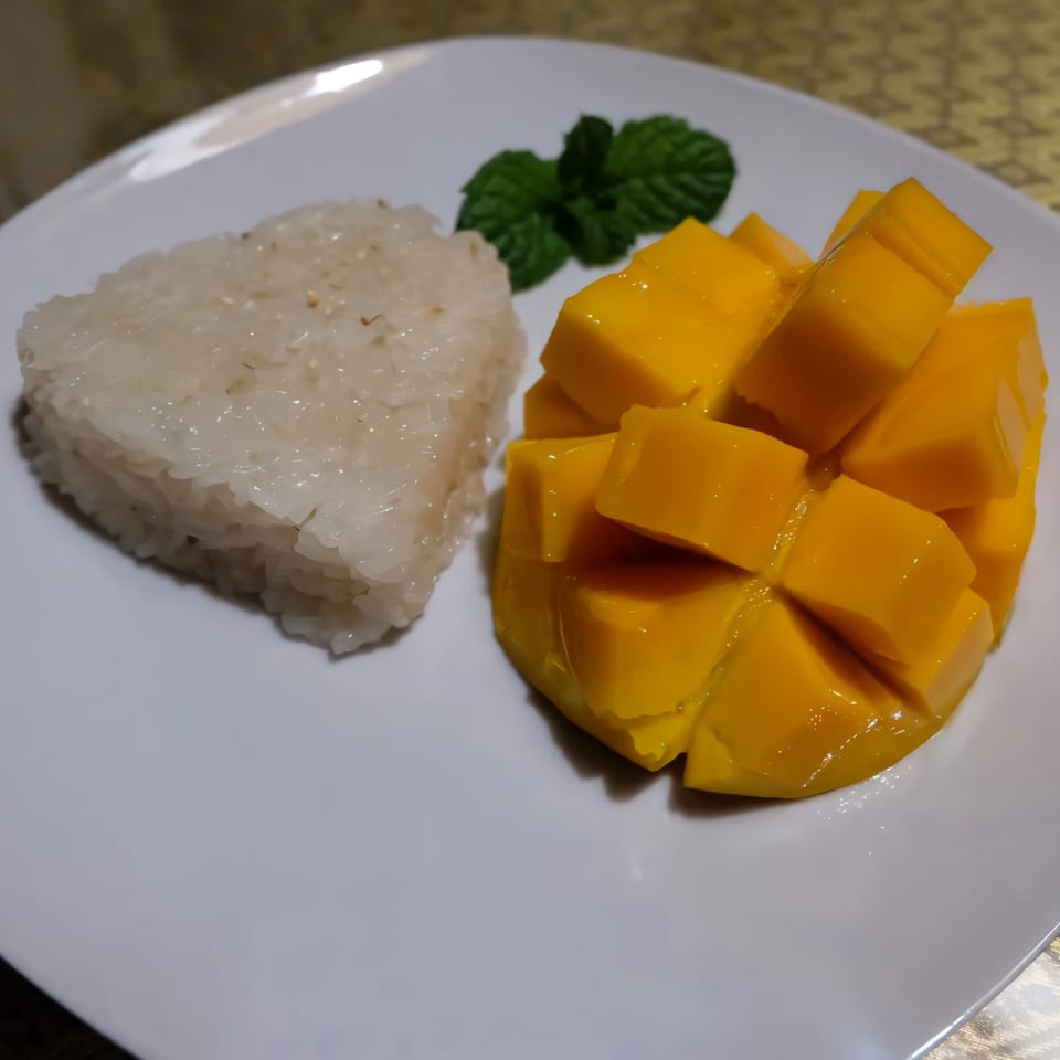 Mango sticky rice dessert with fresh mint on a white plate at Thai Nakornping Restaurant.
