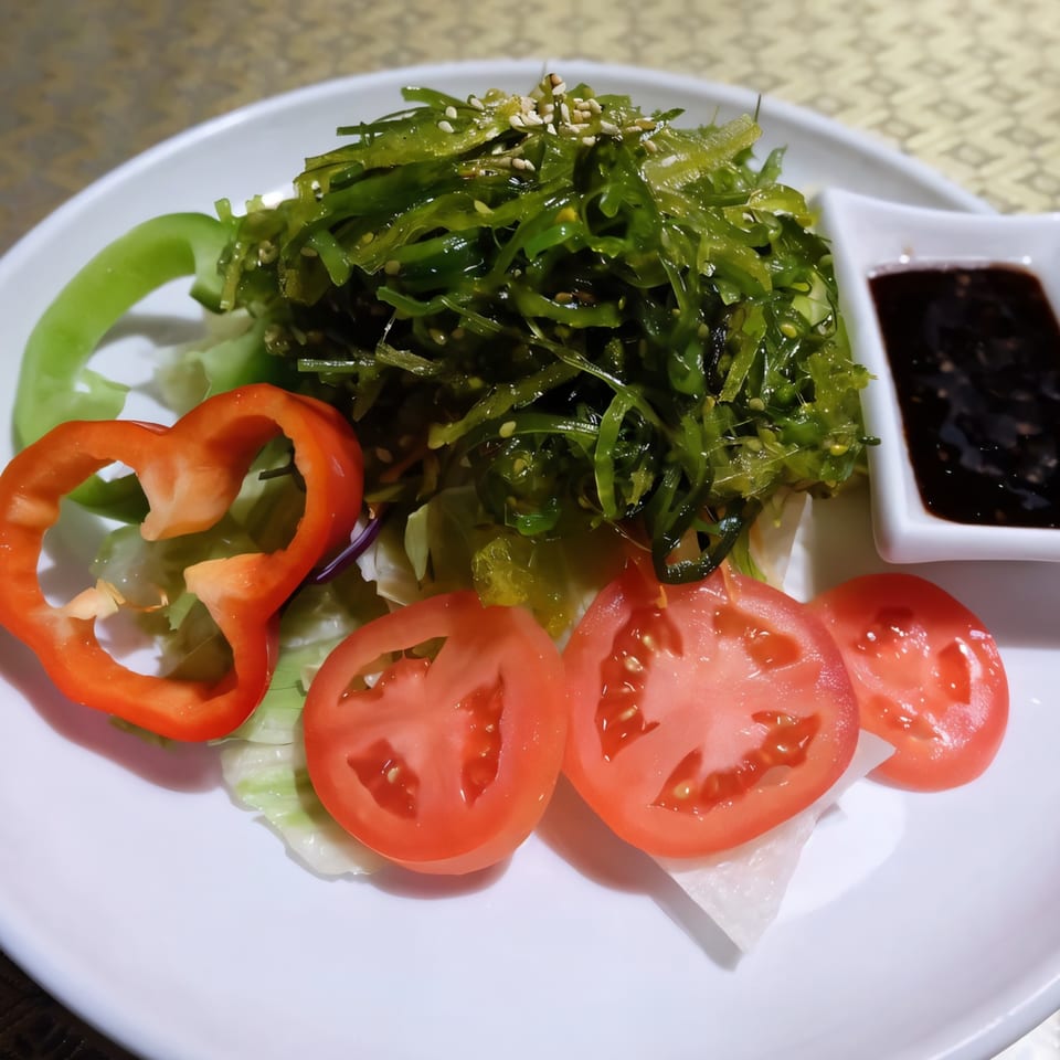 A Thai seaweed salad with tomatoes, bell peppers, and a side of dark sauce.