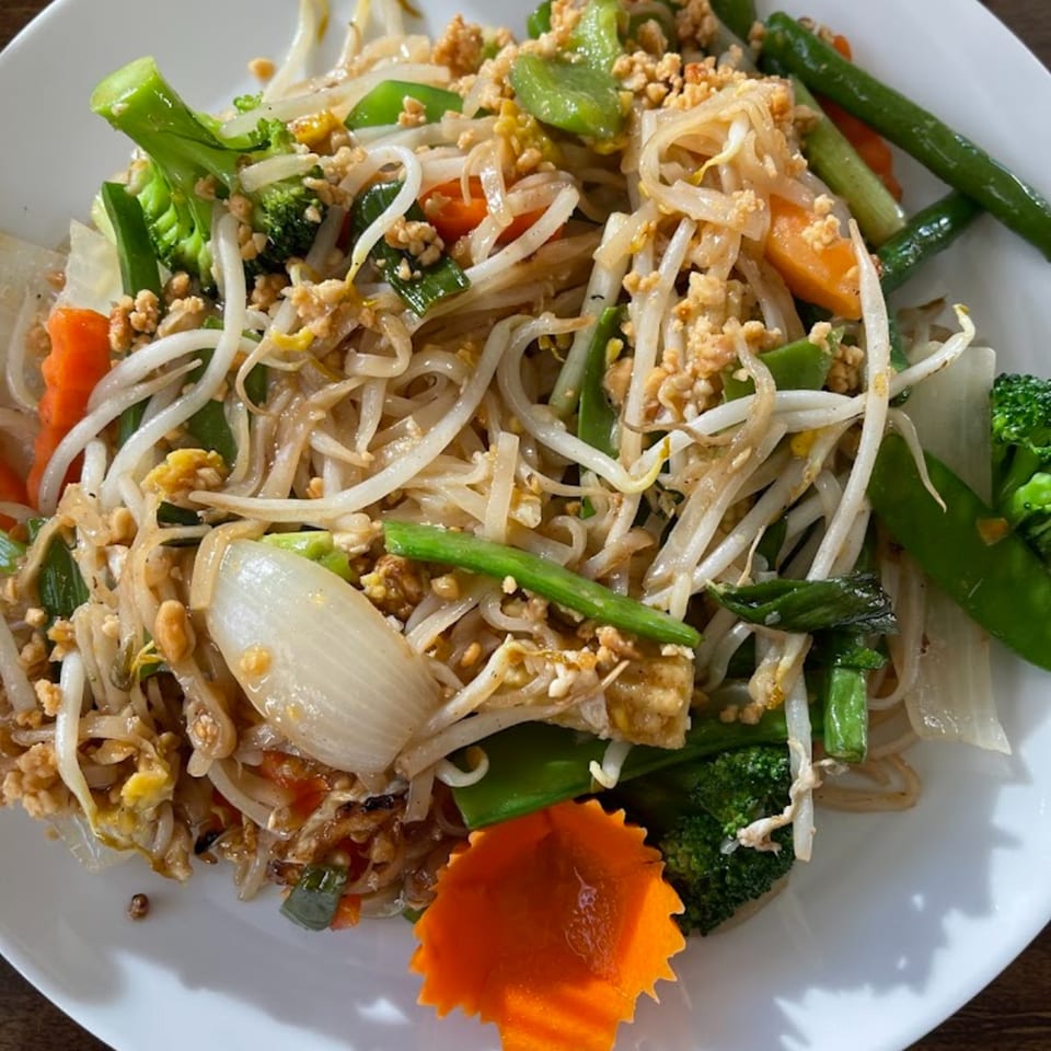Close-up of a Thai dish with noodles, bean sprouts, broccoli, carrots, and ground meat.