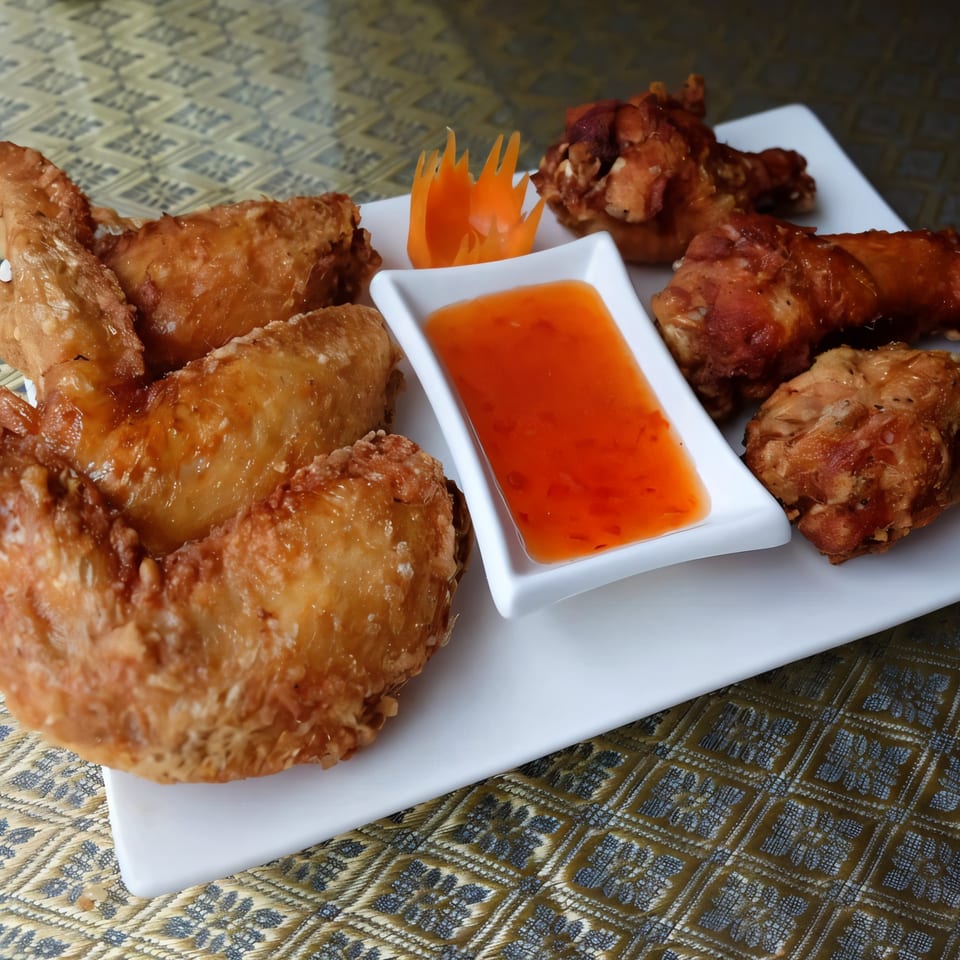 Crispy fried Thai chicken wings with sweet chili dipping sauce and a carrot garnish on a white plate.