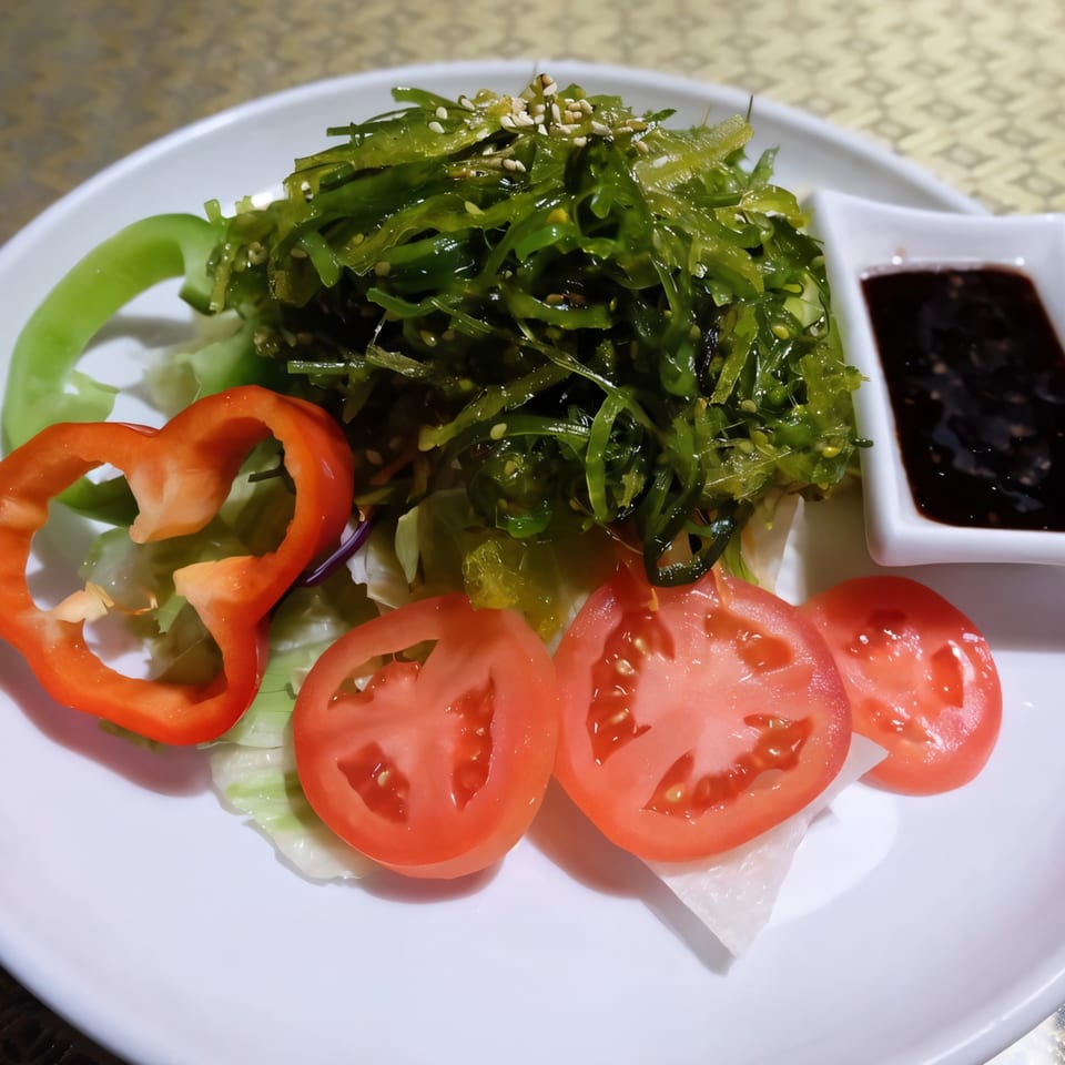 A Thai seaweed salad with tomatoes, bell peppers, and a side of dark sauce on a white plate.